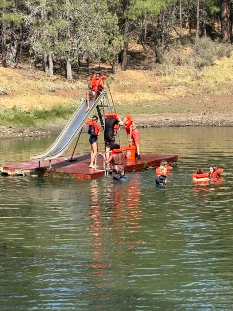 Camp Quest Arizona campers wearing life jackets enjoy swimming and dock activities at a lake