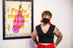 Sophie Mctear standing in front of their "Pride Started as a Riot" Poster