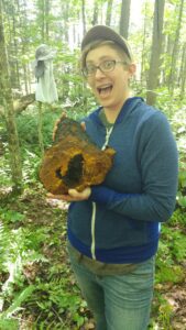 Sarah Baracks holding a log stump in the forest