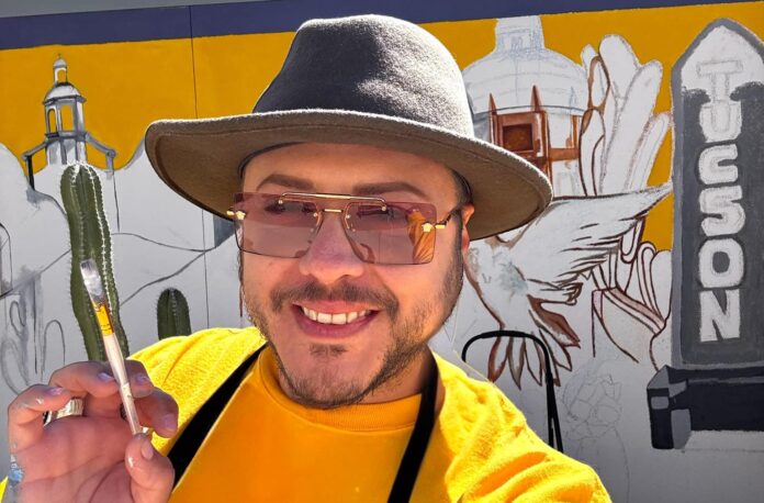 Victor Navarro smiling while painting a colorful Tucson mural, inviting the community to join his Sip & Paint experience at Tucson Gallery.